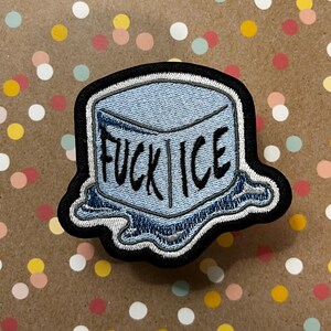 May include: Embroidered patch with the words "FUCK ICE" in black on a light blue ice cube design. The patch has a black border and a melting ice effect at the bottom. The background is a speckled pattern.