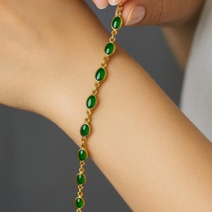 Op de afbeelding: Een gouden kettingarmband met ovale, groene edelstenen.