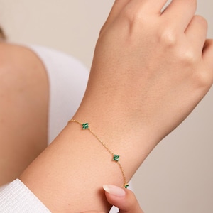 May include: A gold chain bracelet with small green gemstone accents. The bracelet features a delicate chain and four small square-shaped gemstones.