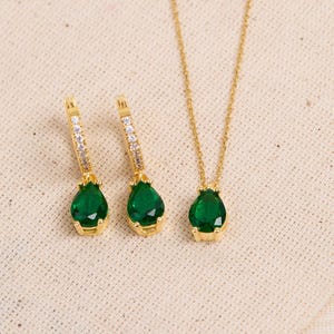 May include: A gold necklace and earrings set with teardrop-shaped green gemstones and clear cubic zirconia accents.