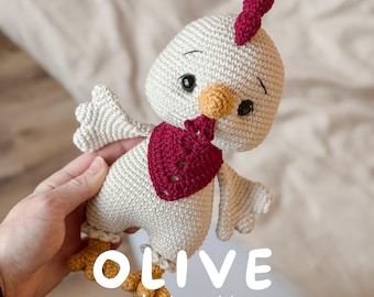 May include: A cream-colored crochet chicken toy with a dark red comb, wattle, and neck scarf. The chicken has yellow feet, a yellow beak, and black safety eyes. The text OLIVE crochet pattern is printed in white over the lower portion of the toy.