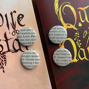 May include: Four circular buttons with text from a book are displayed on two books. The buttons have a white background with black text. The books have maroon and tan covers. The buttons are a literary theme.
