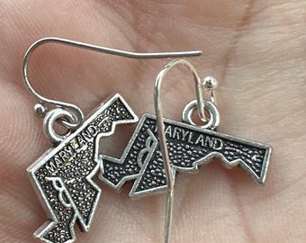 May include: Silver earrings shaped like the state of Maryland with the word "Maryland" written on them.