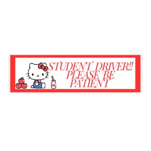 Puede incluir: Un cartel rojo y blanco de conductor estudiante con un personaje de dibujos animados de Hello Kitty sosteniendo una manzana. El cartel dice "STUDENT DRIVER!! PLEASE BE PATIENT"