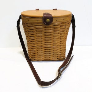 May include: A brown wicker basket with a lid and a brown leather strap. The basket is made of woven wicker and has a natural wood finish.