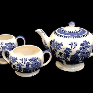 May include: A blue and white porcelain teapot, creamer, and sugar bowl set with a traditional willow pattern.