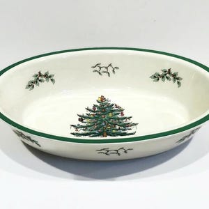 May include: A white oval ceramic baking dish with a green rim. The dish features a green and brown Christmas tree design.
