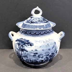 May include: A white ceramic mug with a black handle and the text "But first, coffee" in a black, handwritten-style font. The mug is on a white surface.