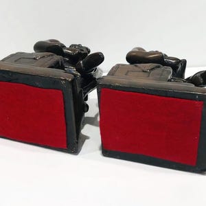 May include: A pair of bronze bookends featuring a seated figure with a book. The bookends have a red felt base.