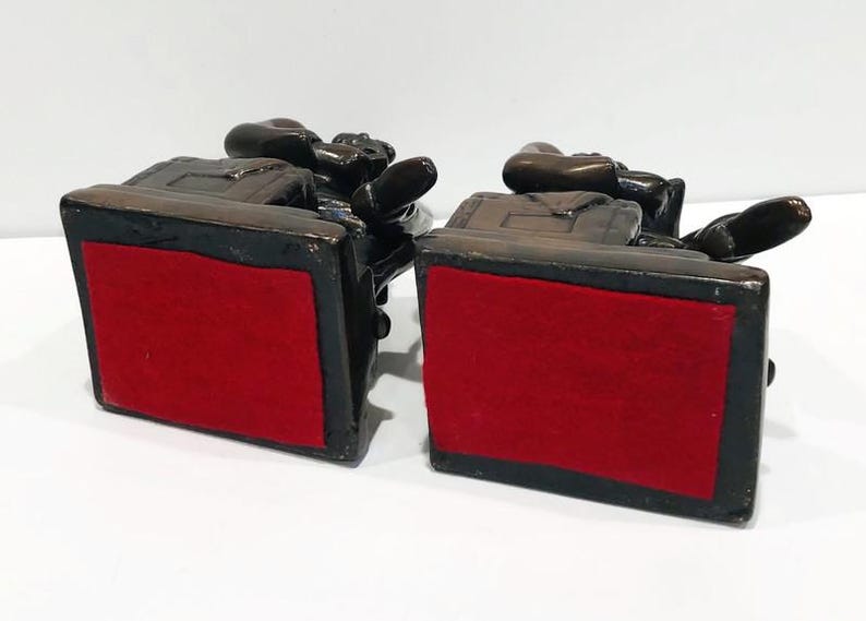 May include: A pair of bronze bookends featuring a seated figure with a book. The bookends have a red felt base.