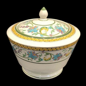 May include: White ceramic sugar bowl with a lid. The bowl and lid are decorated with a floral pattern in shades of blue, green, yellow, and purple. The bowl has a footed base.