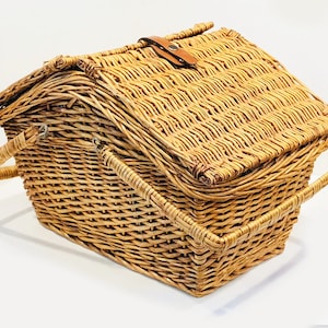 May include: A woven wicker picnic basket with a hinged lid and two handles. The basket is made of natural brown wicker and has a leather strap closure.
