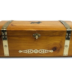 May include: A wooden chest with brass accents and a silhouette of a dog on the lid. The chest has a hinged lid and a brass lock.