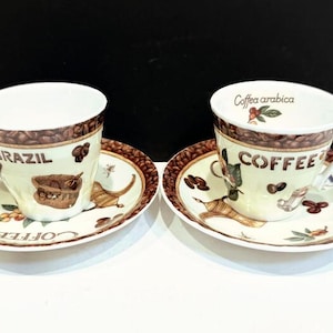 May include: Two matching coffee cups and saucers. The cups have a white interior and a brown band of coffee beans around the rim. The saucers and cups have a light green background with coffee-themed illustrations and the words "BRAZIL" and "COFFEE".
