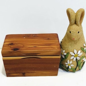 May include: A wooden box with the inscription "Leach Lake Walker, Minn." on the top. The box is next to a ceramic rabbit figurine decorated with white daisies.