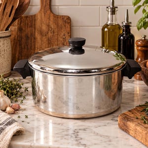 May include: A polished stainless steel cooking pot with a matching lid, featuring two black side handles and a black knob on the lid. The pot has a cylindrical shape with a flat base and a reflective, metallic finish, designed for stovetop use.