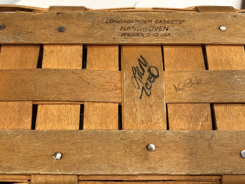 May include: A close-up of a wooden basket with the text "Longaberger Baskets" and "Handwoven Dresden O-O USA" printed on the top. The basket is made of natural wood and has a woven pattern. The text "July 2000" is handwritten on the basket.