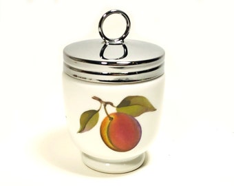 May include: A white ceramic egg coddler with a polished chrome lid featuring a circular handle. The body of the vessel is decorated with a colorful illustration of a single peach with green leaves attached to a small brown stem on the front side.