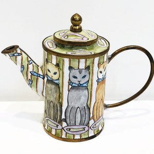 May include: A green and white striped teapot with a gold lid and handle. The teapot is decorated with three cats wearing blue bow ties and surrounded by fish.