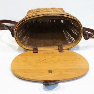 May include: A brown wicker basket with a leather strap and a wooden lid. The lid has a brass latch and the inscription "Maine Guide" is visible on the inside of the lid.