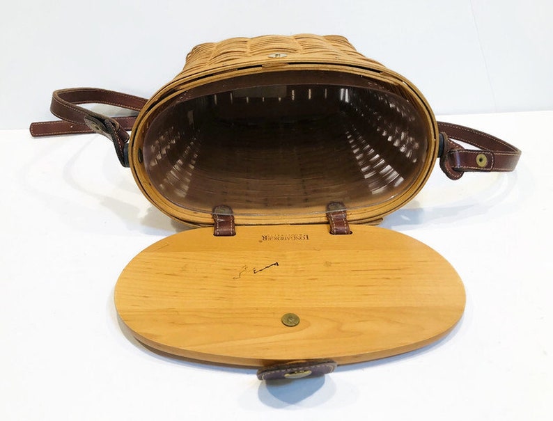 May include: A brown wicker basket with a leather strap and a wooden lid. The lid has a brass latch and the inscription "Maine Guide" is visible on the inside of the lid.