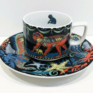 May include: A black and white ceramic teacup and saucer set with a colorful monkey and starfish design. The cup has a white interior and a black rim. The saucer has a black rim and a white interior.