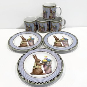 May include: Set of four blue and white mugs and three white plates with a bunny holding a basket of Easter eggs. The plates have a checkered border and a light blue stripe.