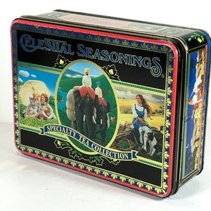 May include: A rectangular Celestial Seasonings Specialty Tea Collection tin. The black tin features colorful illustrations of people, elephants, and landscapes. The top of the tin has the words "Celestial Seasonings" in gold lettering.