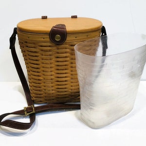 May include: A brown wicker basket with a leather strap and a clear plastic liner. The basket has a lid and is designed to be carried on the shoulder.
