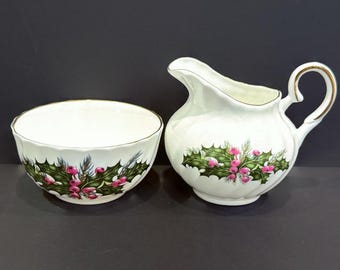 May include: A white porcelain sugar bowl and creamer set with a green holly and pink berry design.