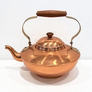 May include: A copper kettle with a wooden handle and brass accents. The kettle has a rounded body and a spout on the side.