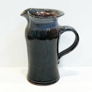 May include: A dark blue and brown ceramic pitcher with a handle. The pitcher has a slightly flared lip and a rounded body.