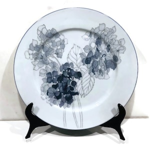 May include: A white porcelain dinner plate with a black and white floral design. The design features hydrangeas with detailed leaves and stems.