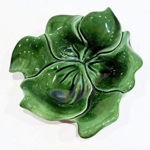 May include: A glossy, green ceramic serving dish shaped like a stylized flower. The dish has multiple sections, each resembling a petal. The vibrant green color and unique design make it a decorative and functional piece for serving snacks or small dishes.