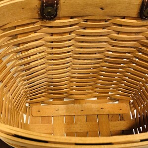 May include: A woven wicker basket with leather handles. The basket is empty and the inside is visible.