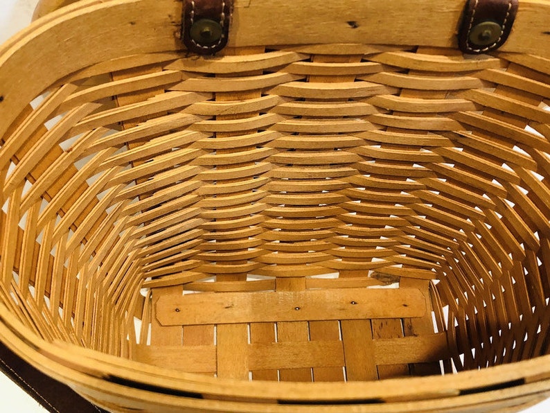 May include: A woven wicker basket with leather handles. The basket is empty and the inside is visible.