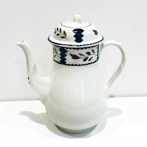 May include: White ceramic coffee pot with a blue and green floral design. The pot has a lid and a spout.