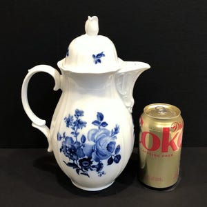 May include: White porcelain coffee pot with a blue floral design. The pot has a lid and a handle. It is next to a can of caffeine-free soda for size comparison.
