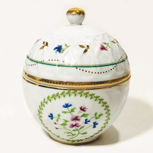 May include: A white porcelain lidded jar with gold trim and a gold knob. The jar features a floral design with blue and pink flowers, and a green and gold band around the middle. The lid has a textured pattern.