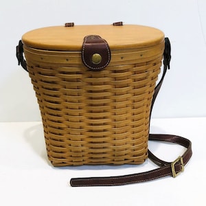May include: A woven wicker basket with a brown leather strap and a wooden lid. The basket has a brown leather handle and a brass buckle.