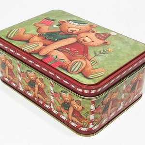 May include: Red and green tin box with a Christmas theme. The lid features two teddy bears wearing Santa hats and holding gifts. The sides of the box are decorated with a repeating pattern of teddy bears wearing Santa hats and candy canes.