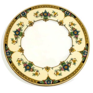 May include: A white ceramic plate with a gold and black border and a floral design in shades of blue, yellow, and pink.