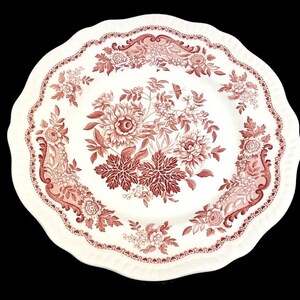 May include: White ceramic plate with a scalloped edge and a floral design in shades of red. The plate features a central bouquet of flowers and leaves, surrounded by smaller floral motifs and decorative borders. A classic, elegant design.