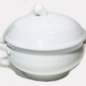 May include: White porcelain soup tureen with a lid and two handles. The tureen has a woven pattern and a decorative knob on the lid.