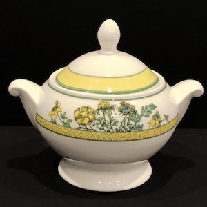 May include: White ceramic sugar bowl with a lid, featuring a floral design with yellow flowers and green leaves. The bowl has a yellow and green trim around the top.