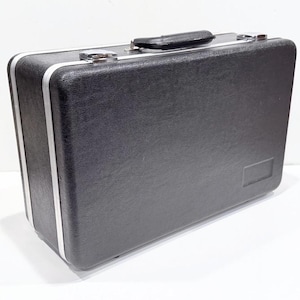 May include: A black rectangular briefcase with a textured surface, silver trim, and a black handle. The case has a rectangular label on the front and is set against a white background.