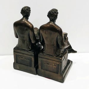May include: A pair of bronze bookends featuring a seated figure of Abraham Lincoln. Each bookend has the word "LINCOLN" inscribed on the base.