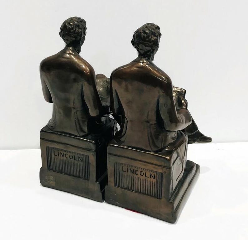 May include: A pair of bronze bookends featuring a seated figure of Abraham Lincoln. Each bookend has the word "LINCOLN" inscribed on the base.