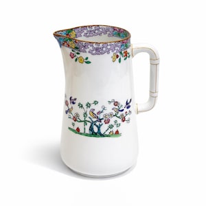 May include: White ceramic pitcher with a decorative floral and bird design. The pitcher features a bamboo-style handle and a colorful floral border around the rim. The design includes birds, flowers, and trees.