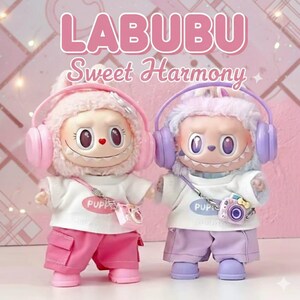 Op de afbeelding: Twee LABUBU Sweet Harmony poppen. De ene pop is roze, de andere paars. Beide poppen dragen een koptelefoon, witte t-shirts en shorts. Elke pop heeft een cameratas. De achtergrond is roze.